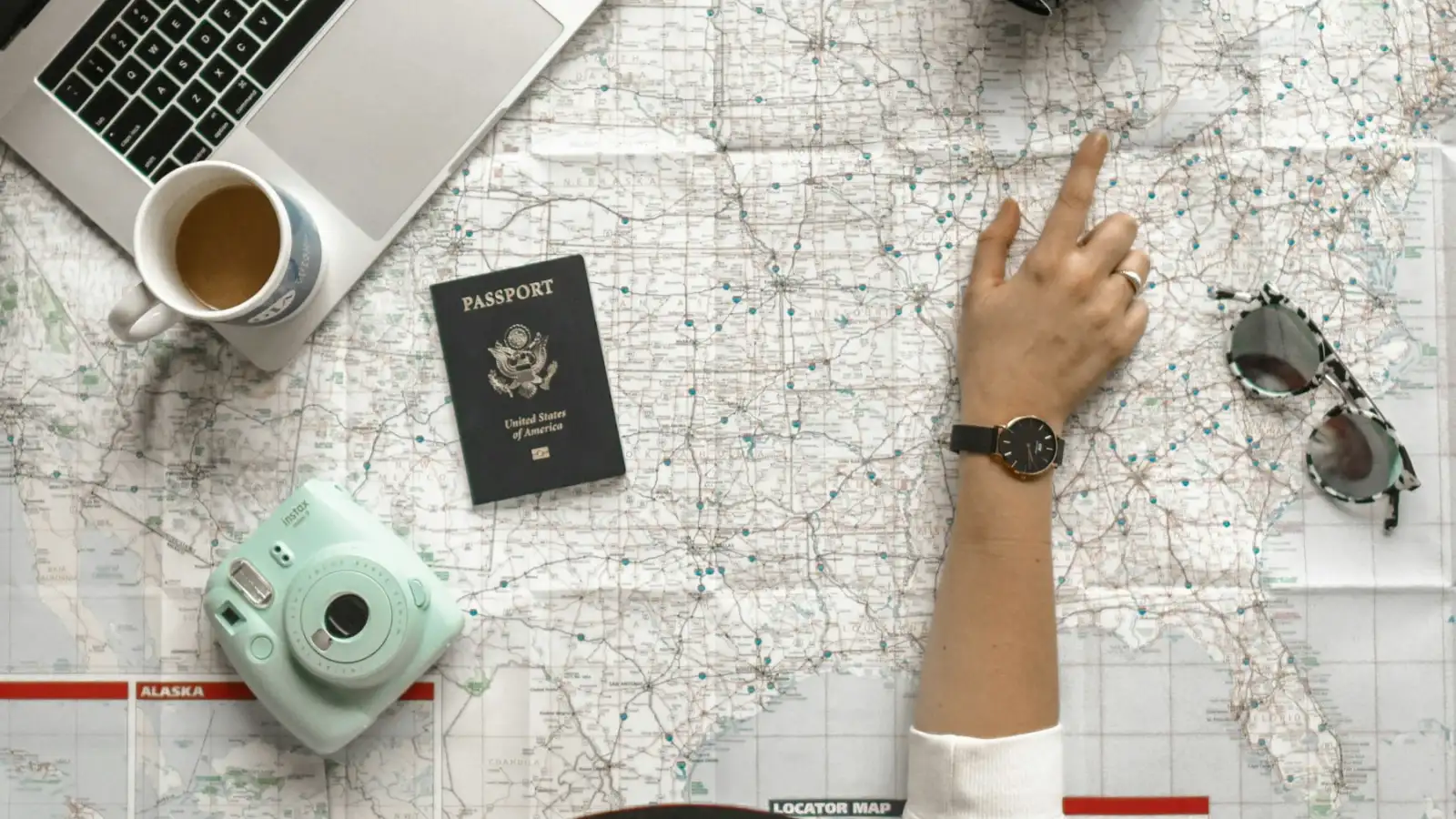 A map of the United States on a desk with a passport, a laptop, and a coffee cup