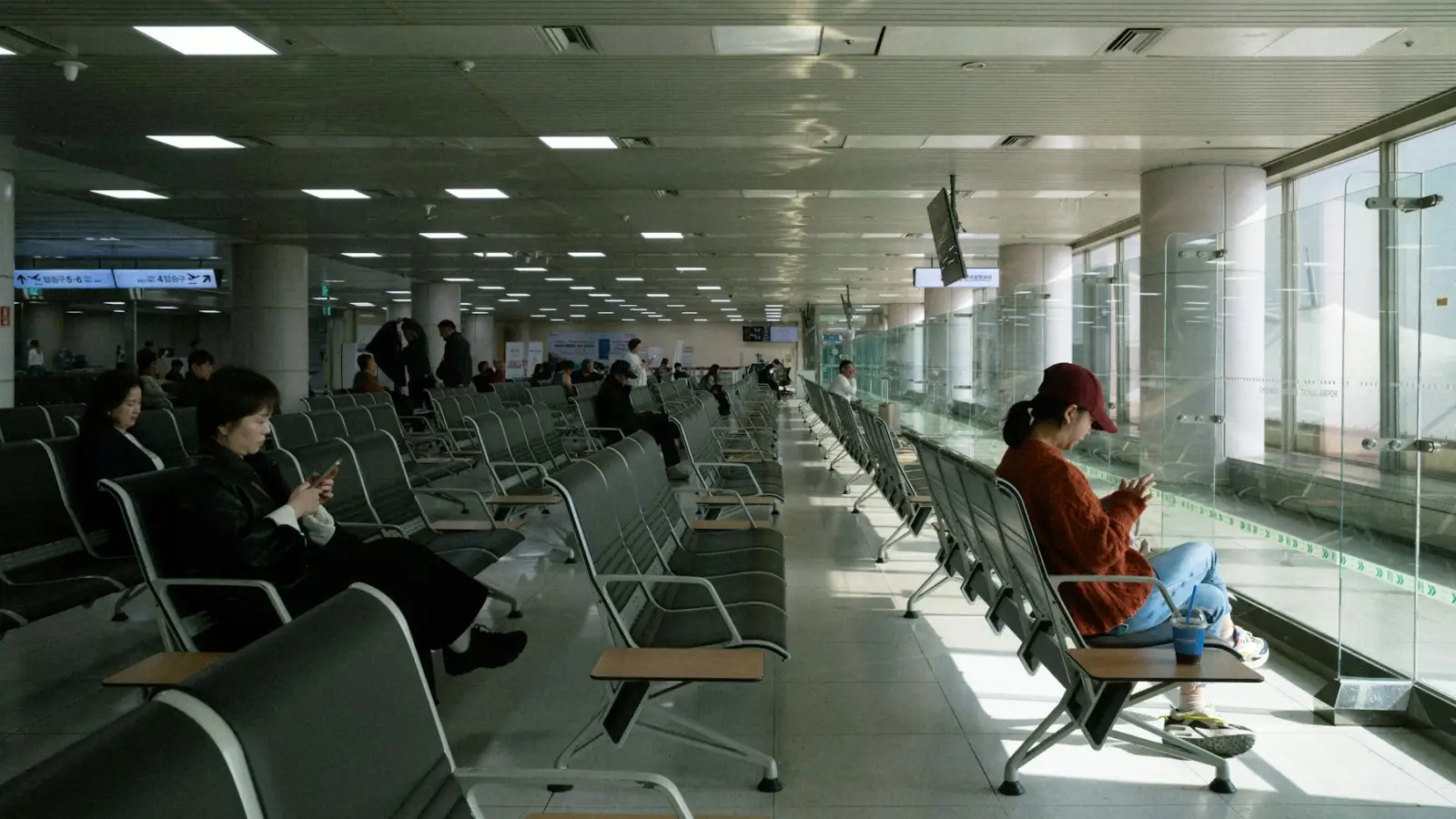 Travelers waiting in a bright airport lounge, one checking a phone
