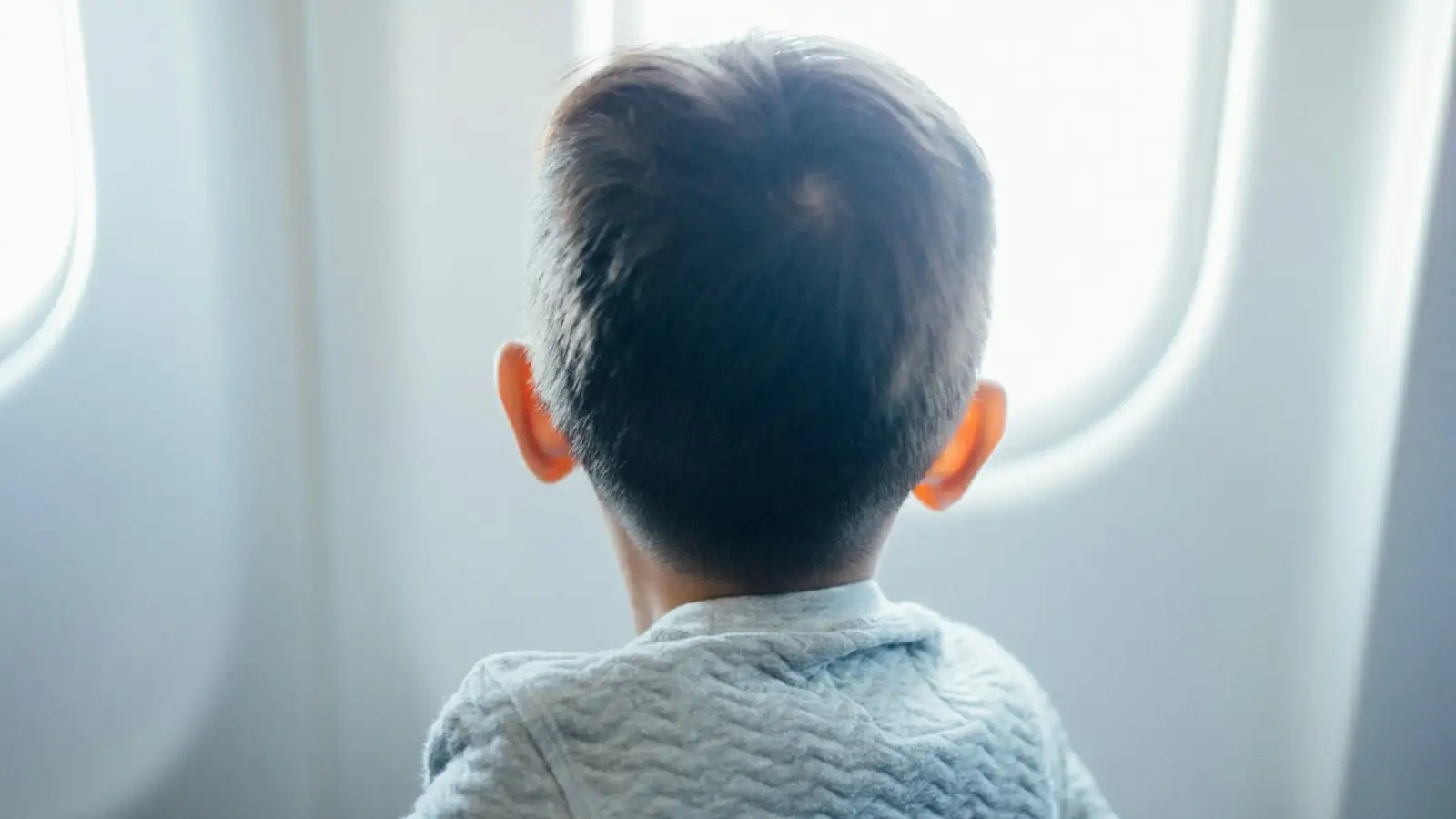 A young boy in an aircraft seat looking out of the cabin window