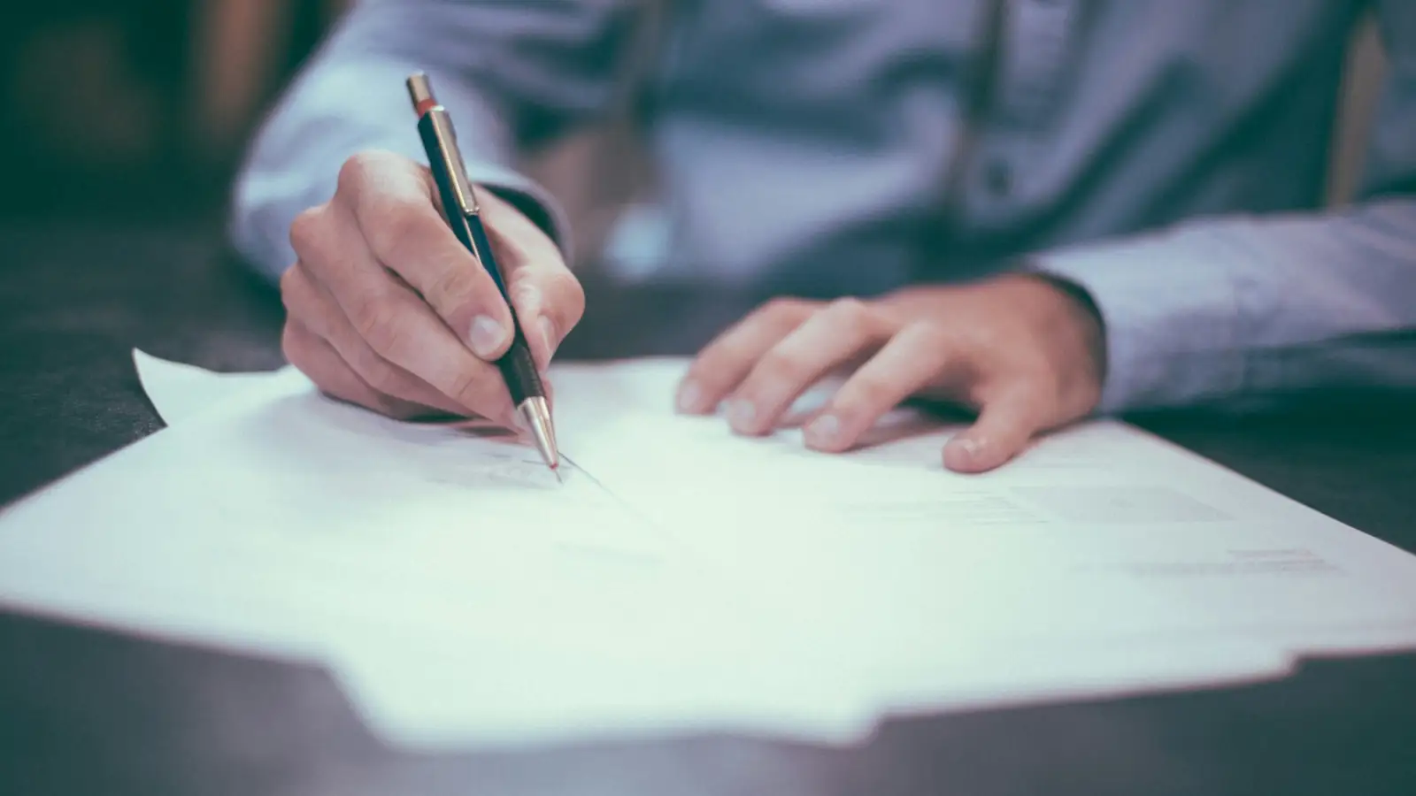 A person reading and signing a document at a desk